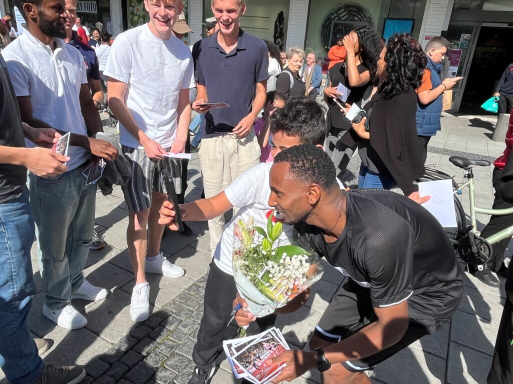 SM-vinnaren Habtom Asgade tar selfie med yngre beundrare på ett torg