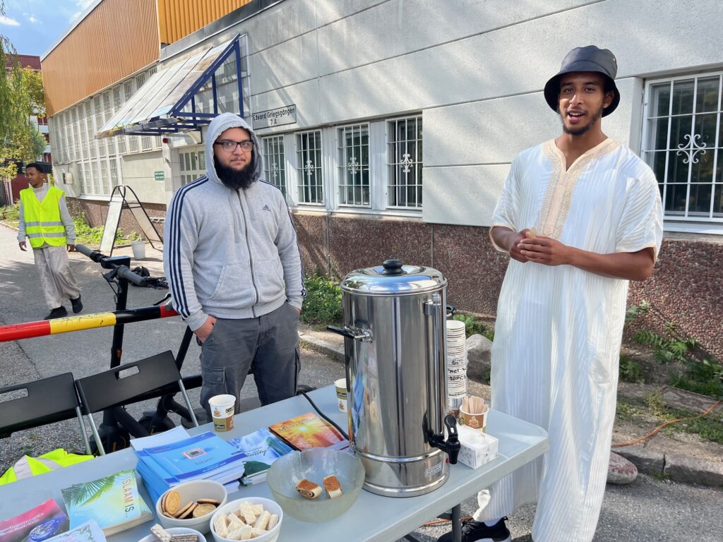 Två unga män framför moskén i Husby bjuder på fika.