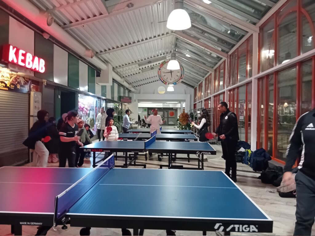 Fyra pingisbord i rad inne i Tensta centrum, barn och vuxna spelar.