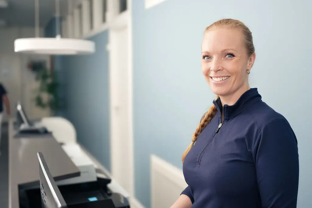 En smilende receptionist byder velkommen ved skranken i klinikken.