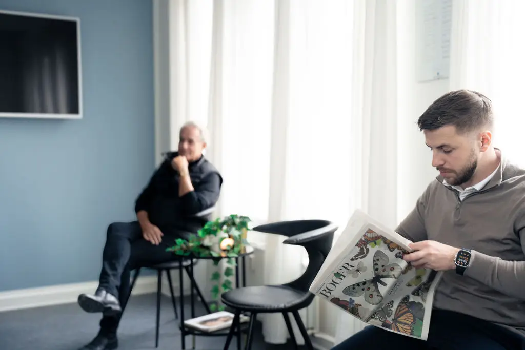 To patienter venter i det lyse og rolige venteværelse hos tandlægerne Ølandshus på Amager. Den ene læser avis, mens den anden slapper af.