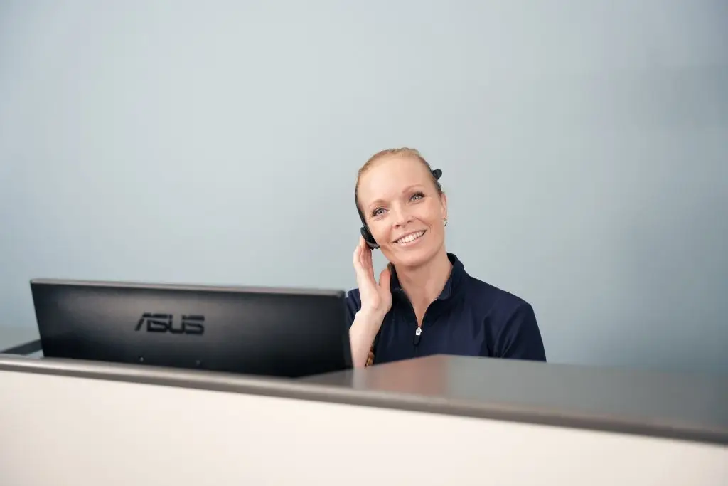 Receptionist taler i telefon og hjælper en patient med booking.