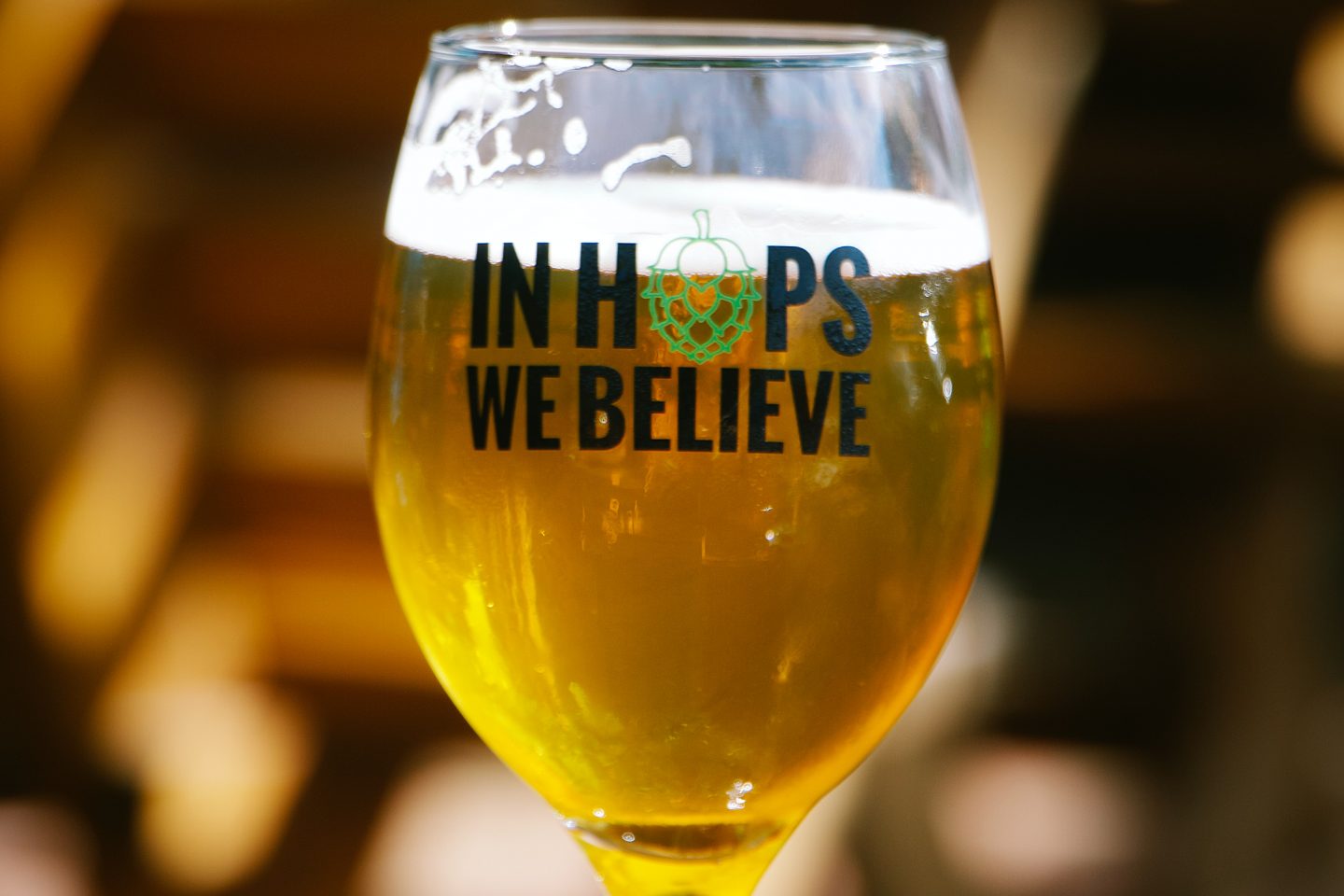 Et glass på bordet fylt med øl. Glasset har teksten "In Hops We Believe"