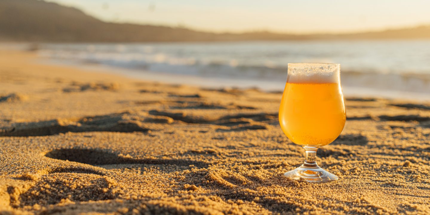 Et glass med øl som står på stranden i solsteiken.