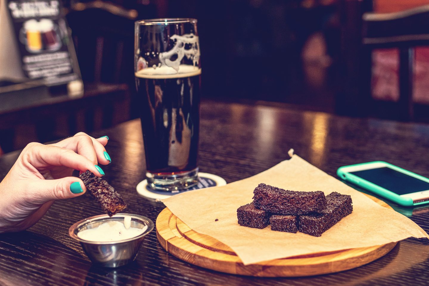 En damehånd som dypper en brownie i en type saus. Flere brownie på bordet på et fat og et glass med mørkt øl (stout) bak.