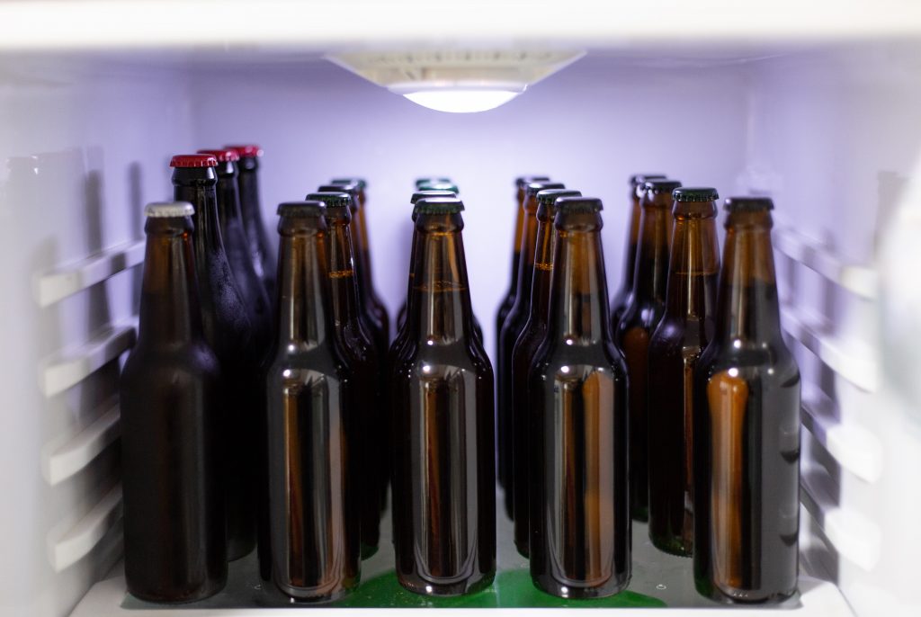 Bilde fra innsiden av et kjøleskap. Vi ser mange brune ølflasker.
