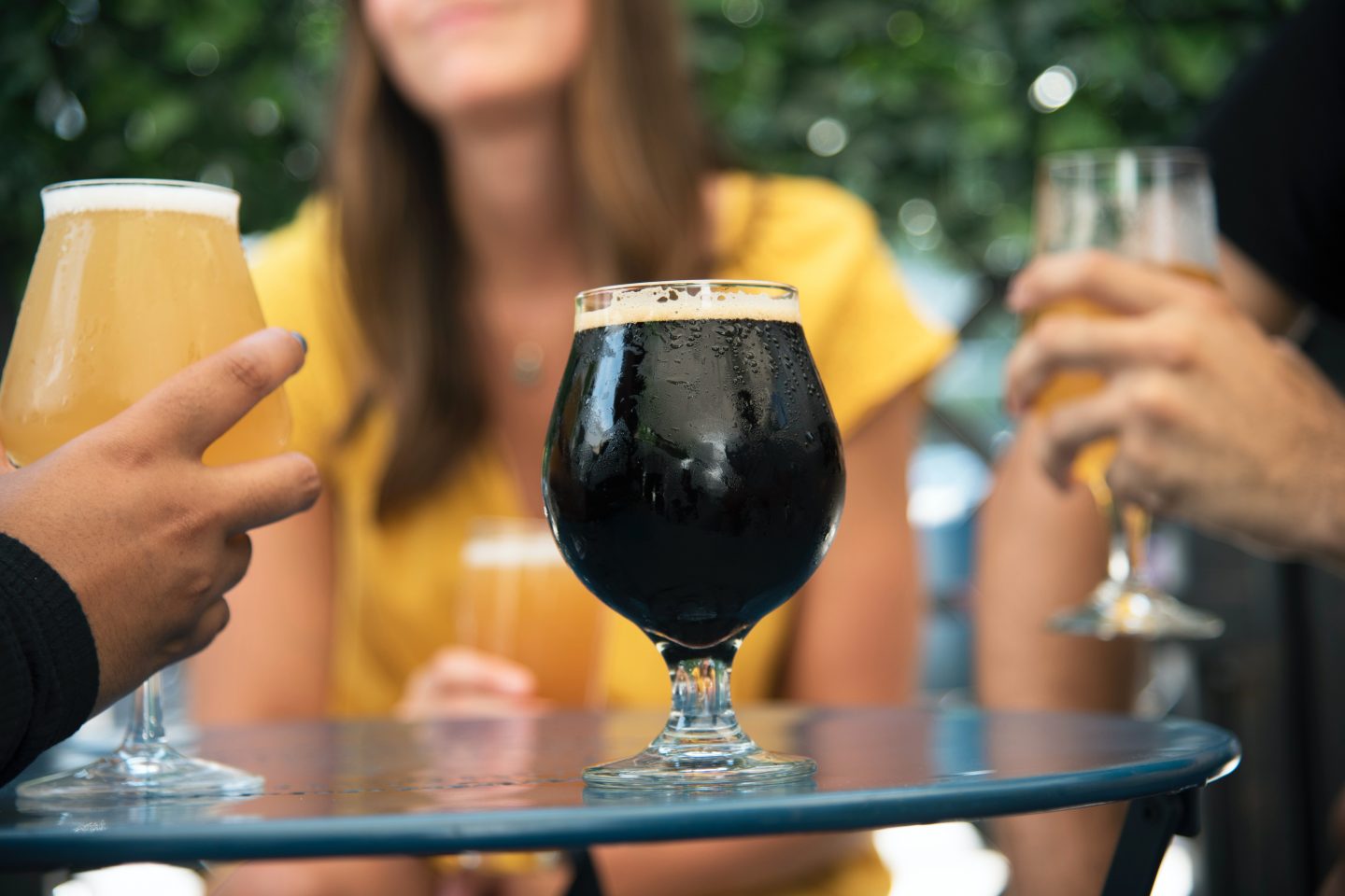 Mange ølglass på et bord med folk rundt. Det midterste glasset er et svart øl.