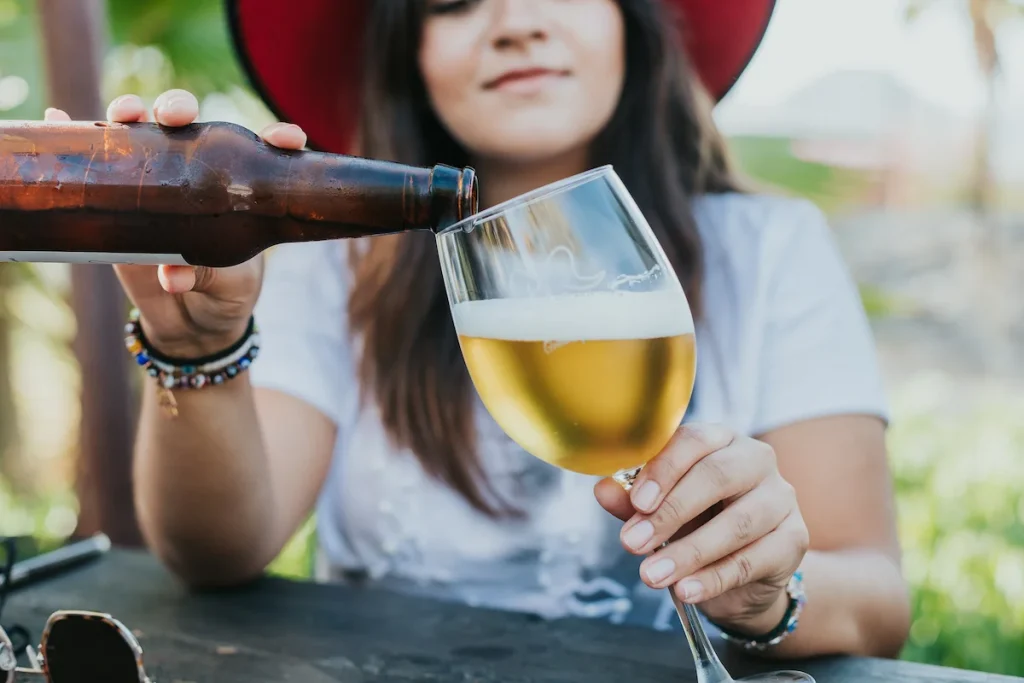 En kvinne med hatt som fyller øl fra en brun flaske i et glass med stett.