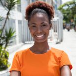 Beautiful african woman in a orange shirt in the city with street, buildings and traffic in the background