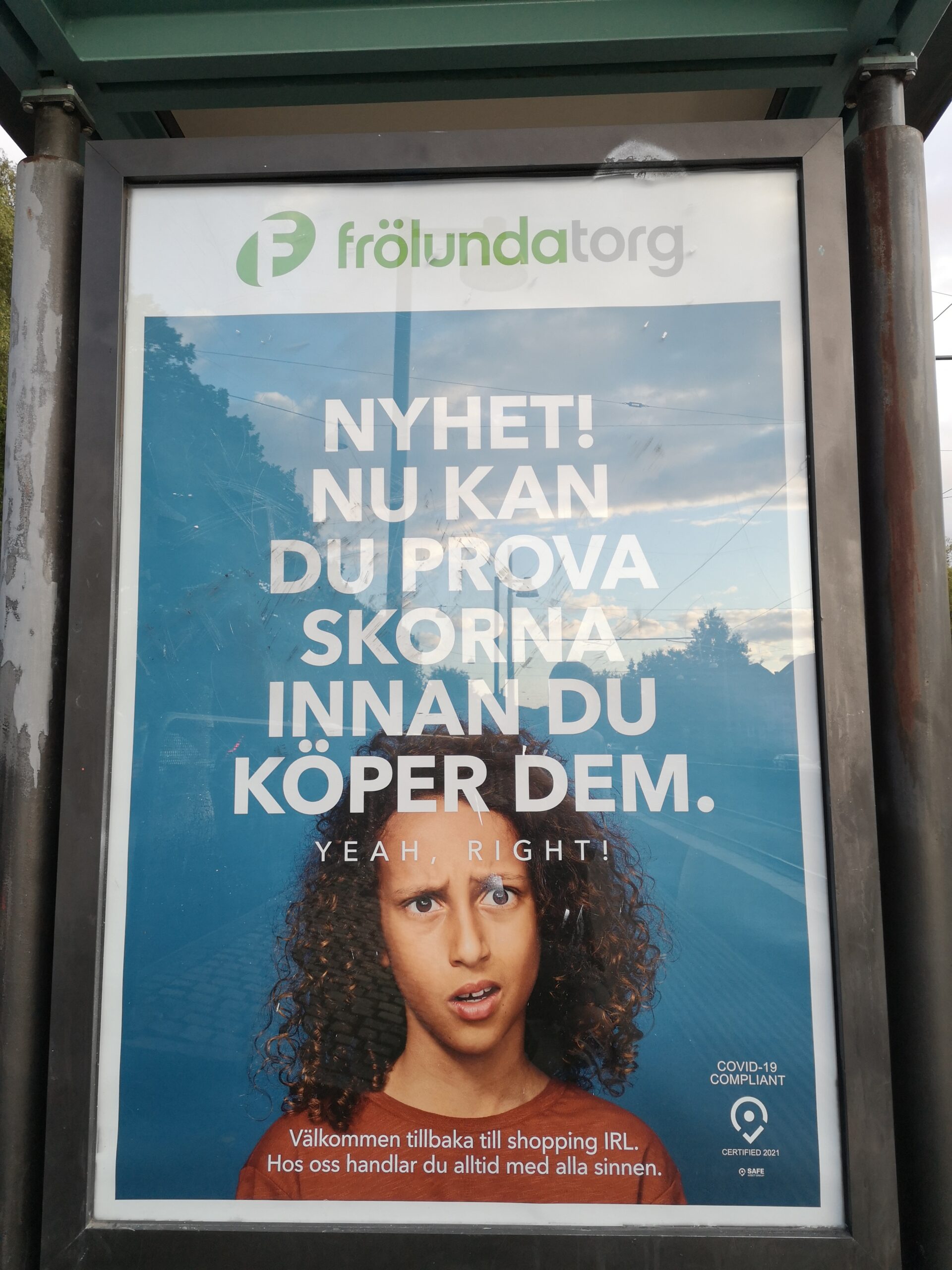 Affisch vid spårvagnshållplats. Under Frölunda torgs logga ett förvånat ansikte och texten "NYHET! NU KAN DU PROVA SKORNA INNAN DU KÖPER DEM"