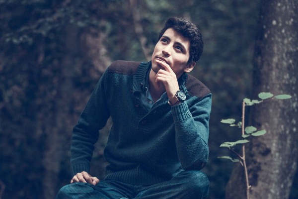 man sitting in the woods wondering something with a hand in front of his mouth