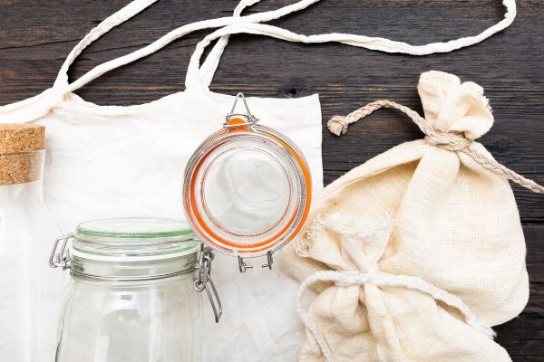 Natural reusable storage options for food, a glass, a cotton bag, and a glass water pitcher.