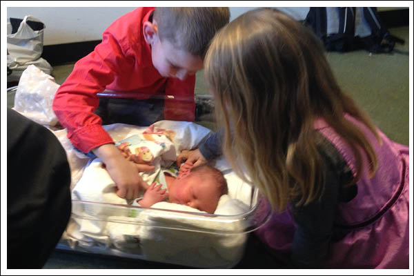 Siblings looking at a newborn baby.