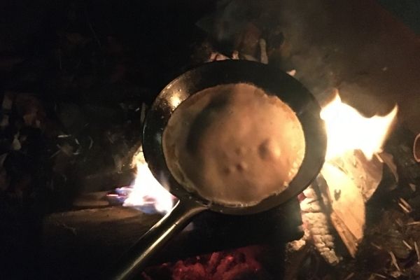 Pancakes cooked over a campfire on a frying pan.