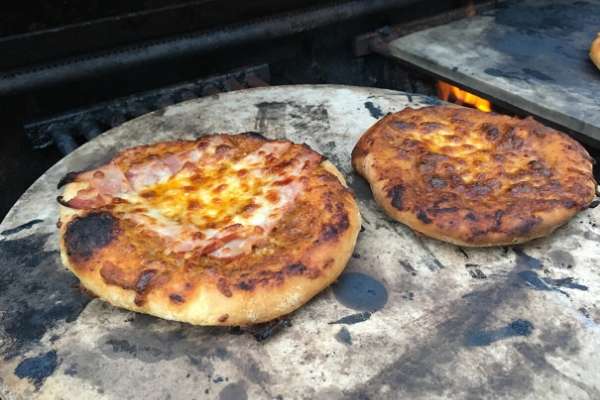 two small pizzas on a pizza stone on an outdoors grill