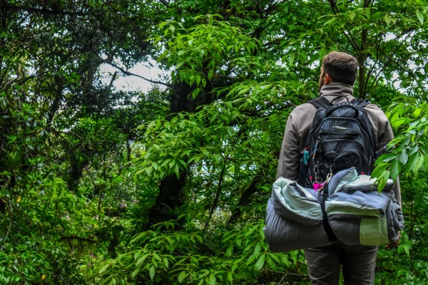 man hiking in the woods with a backpack with a rolled up sleeping bag