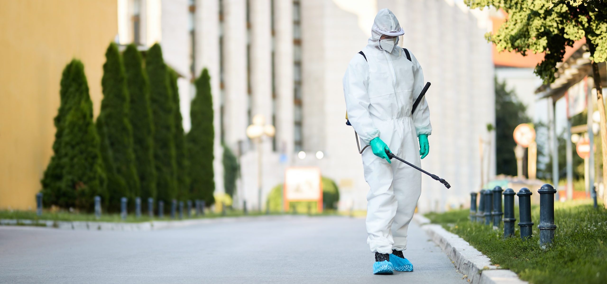 Disinfectant worker in protective suit sanitizing empty city streets during COVID-19 epidemic.