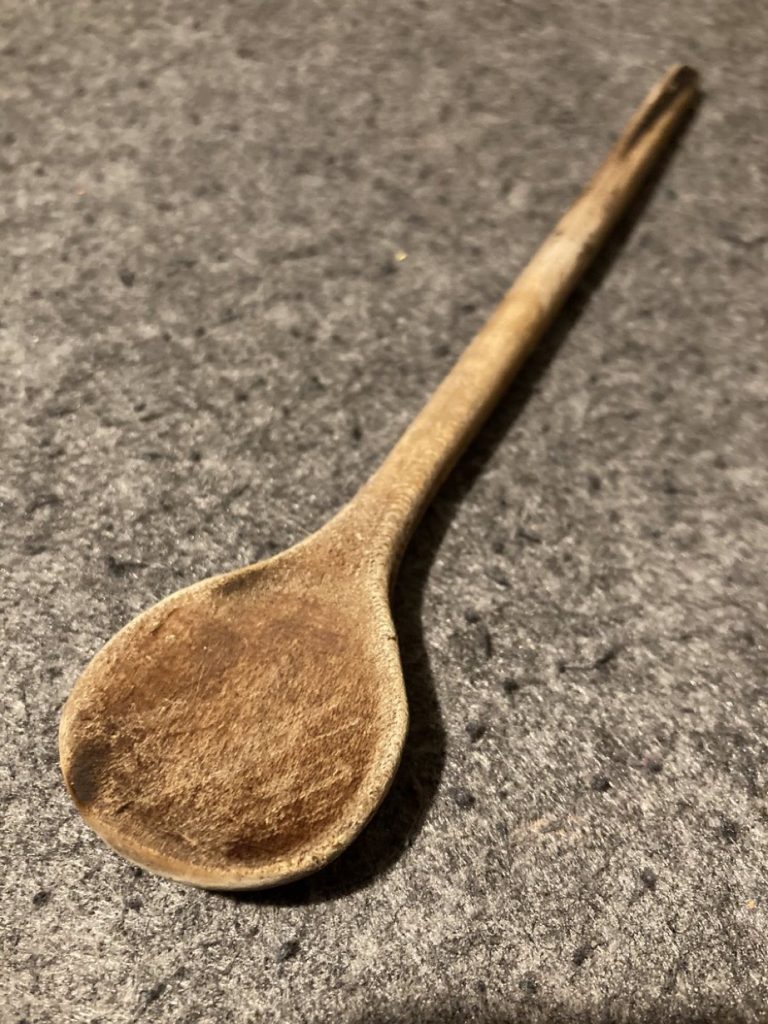 ein stark gebrauchter Holzlöffel auf grauem Filz