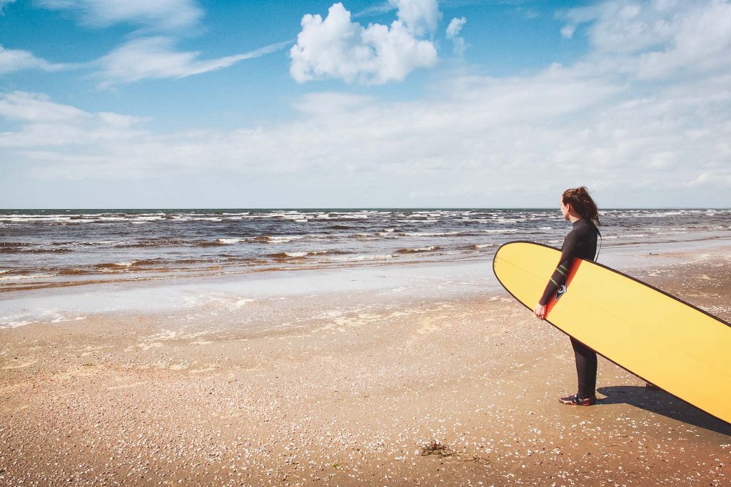 En jente med surfebrett på stranda på Vestkysten av Sverige