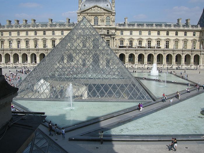 een foto van de glazen piramide met op de achtergrond het zandstenen gebouw van het museum