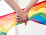 Händer som håller i varandra med Regnbågsflaggan i bakgrunden