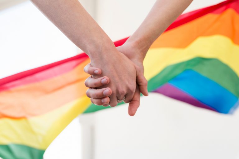 Händer som håller i varandra med Regnbågsflaggan i bakgrunden