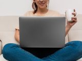 Kvinna med laptop i knät och mugg i handen