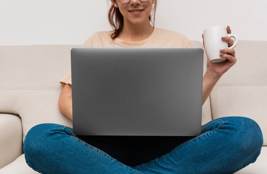 Kvinna med laptop i knät och mugg i handen