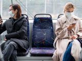 Två kvinnor med munskydd på buss som häller distans till varandra