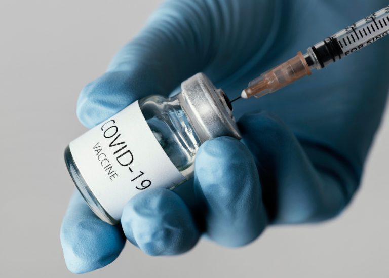 hand i skyddshandske som håller en burk Covid-19 vaccin som laddas i spruta