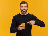 Glad man med mobiltelefon mot gul bakgrund