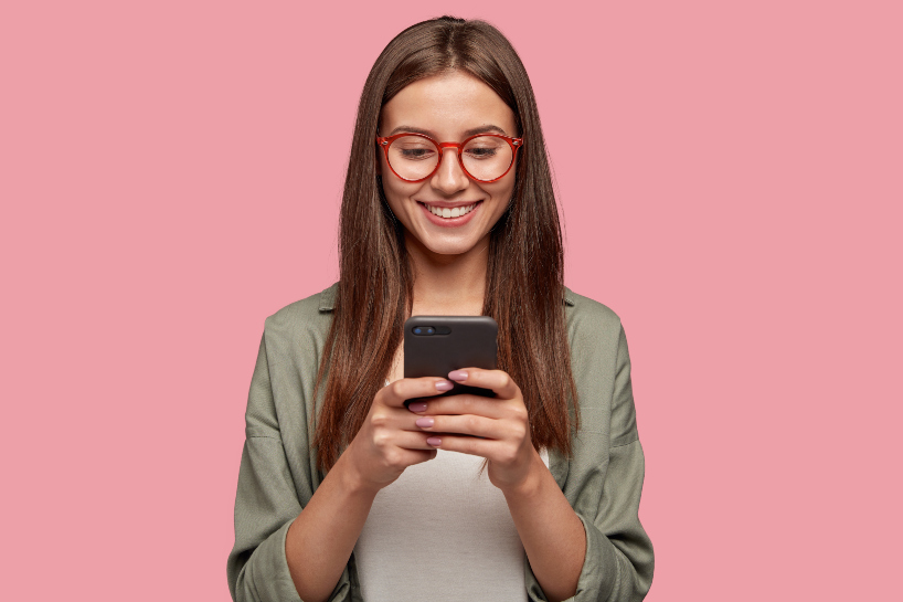 Kvinna med mobiltelefon mot rosa bakgrund