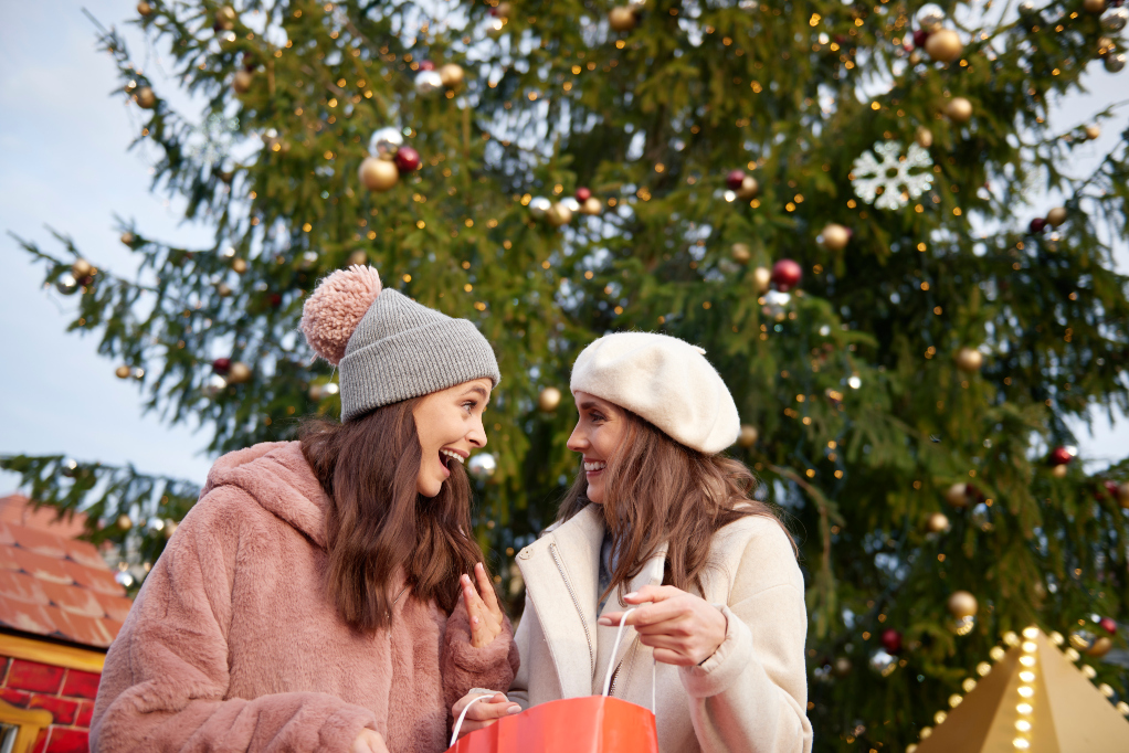 Två kvinnor i ytterkläder framför en julgran ute