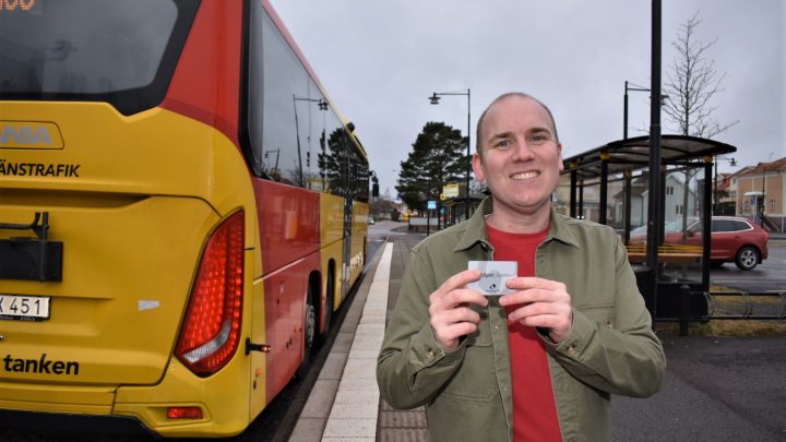 Anton Sejnehed (S) står med ett busskort i handen och en buss bredvid sig och tittar in i kameran