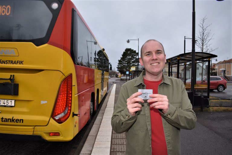 Anton Sejnehed (S) står med ett busskort i handen och en buss bredvid sig och tittar in i kameran