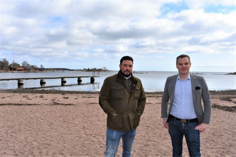 Lucas Lodge (M), kommunalråd i Oskarshamn, och Andreas Erlandsson (S), kommunstyrelsens ordförande i Oskarshamn, står på Havslätts badplats i Oskarshamn och tittar in i kameran