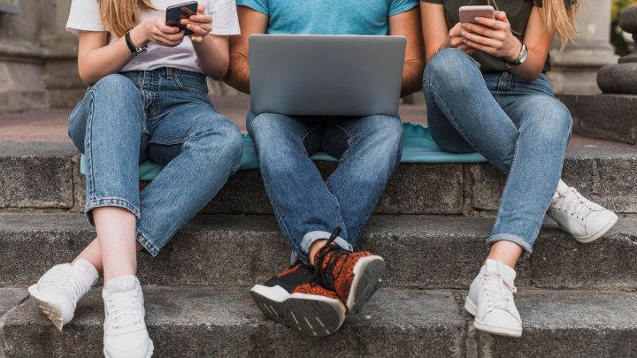 Ungdomar sitter på trappa med mobiler och dator i knät