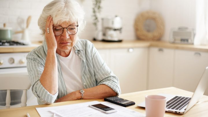 Äldre kvinna sitter vid ett bord och räknar på sin ekonomi
