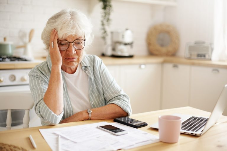 Äldre kvinna sitter vid ett bord och räknar på sin ekonomi
