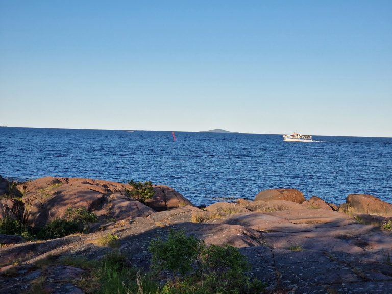 Ernemars klippor i Oskarshamn i förgrunden, Blå Jungfrun i bakgrunden, skärgårdsbåt i Kalmarsund.