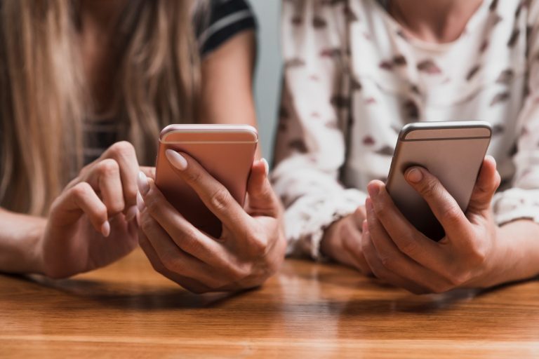 Två kvinnor som scrollar på varsin mobiltelefon