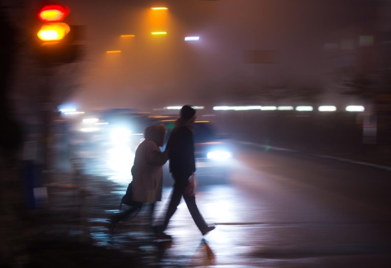 Två personer utan reflex korsar gatan i mörkret