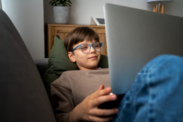 Pojke sitter i soffa med bärbar dator i knät