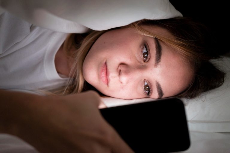 Ung kvinna med mobilen i sängen
