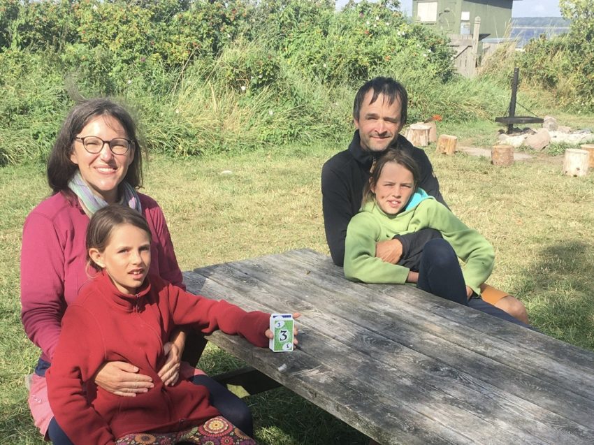 Familie mit zwei Kindern draußen am Tisch.