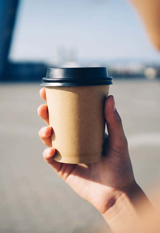 Holder et brunt kaffebæger med sort drikkelåg