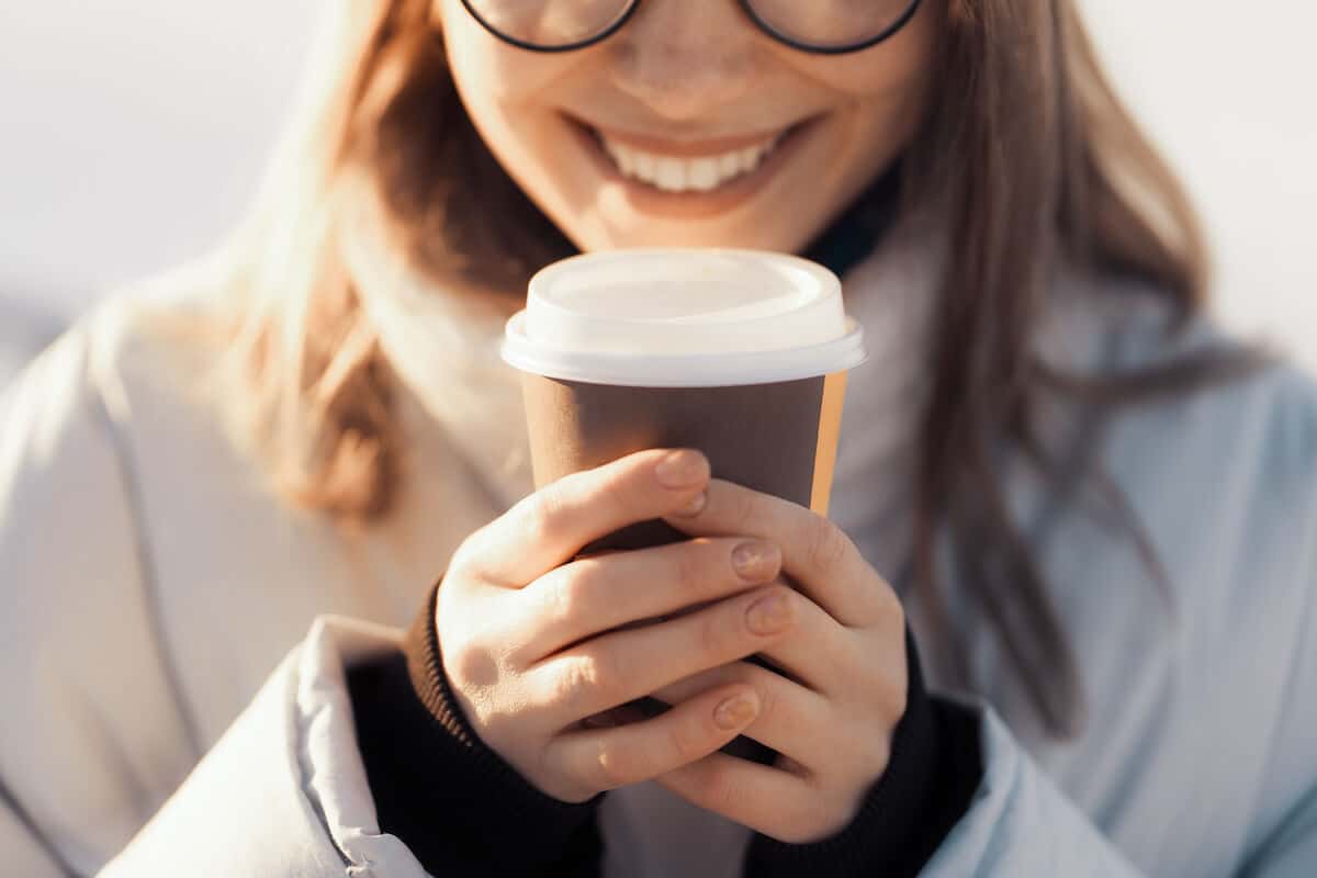 Smilende ung kvinde med en lækker kaffe to go