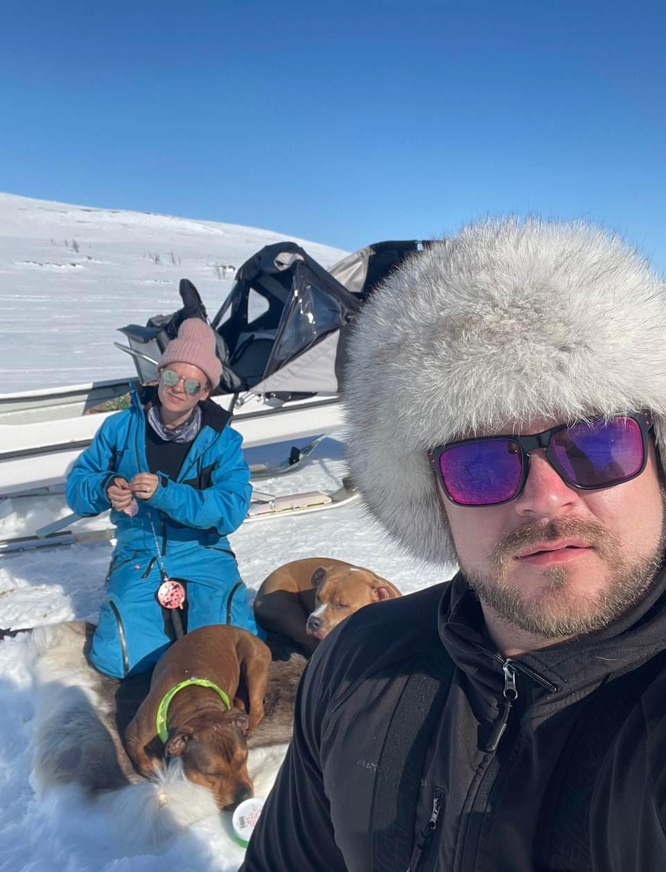 Two people and two dogs outside ice fishing