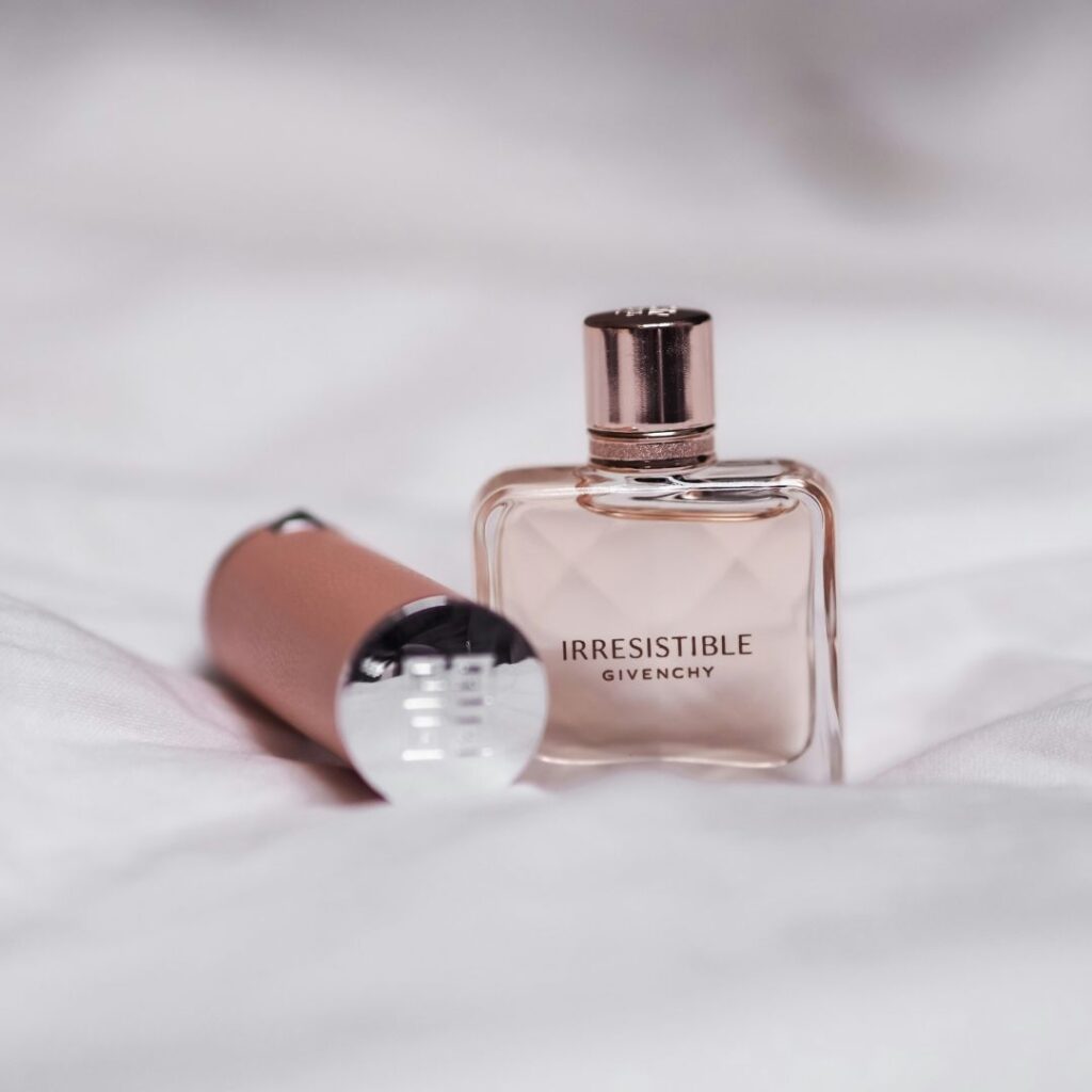 Givenchy parfymen irresistible bredvid ett läppstift utstrålar elegans placerad på ett vitt täcke.