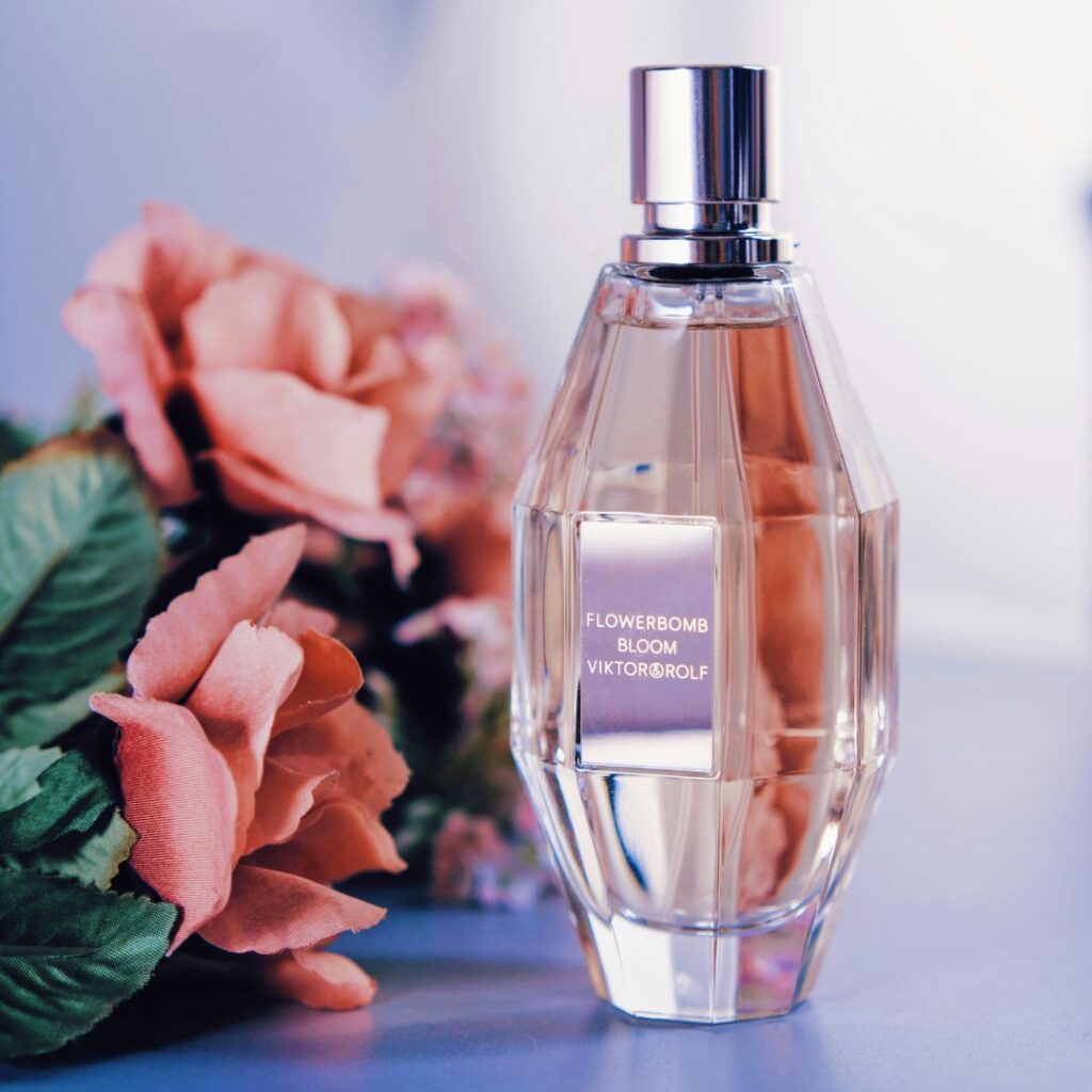 Viktor Rolf Flowerbomb Viktor Rolf Flowerbomb Bloom parfym i rosa parfymflaska och blommor i bakgrund för att symbolisera den blommiga doftnoten.